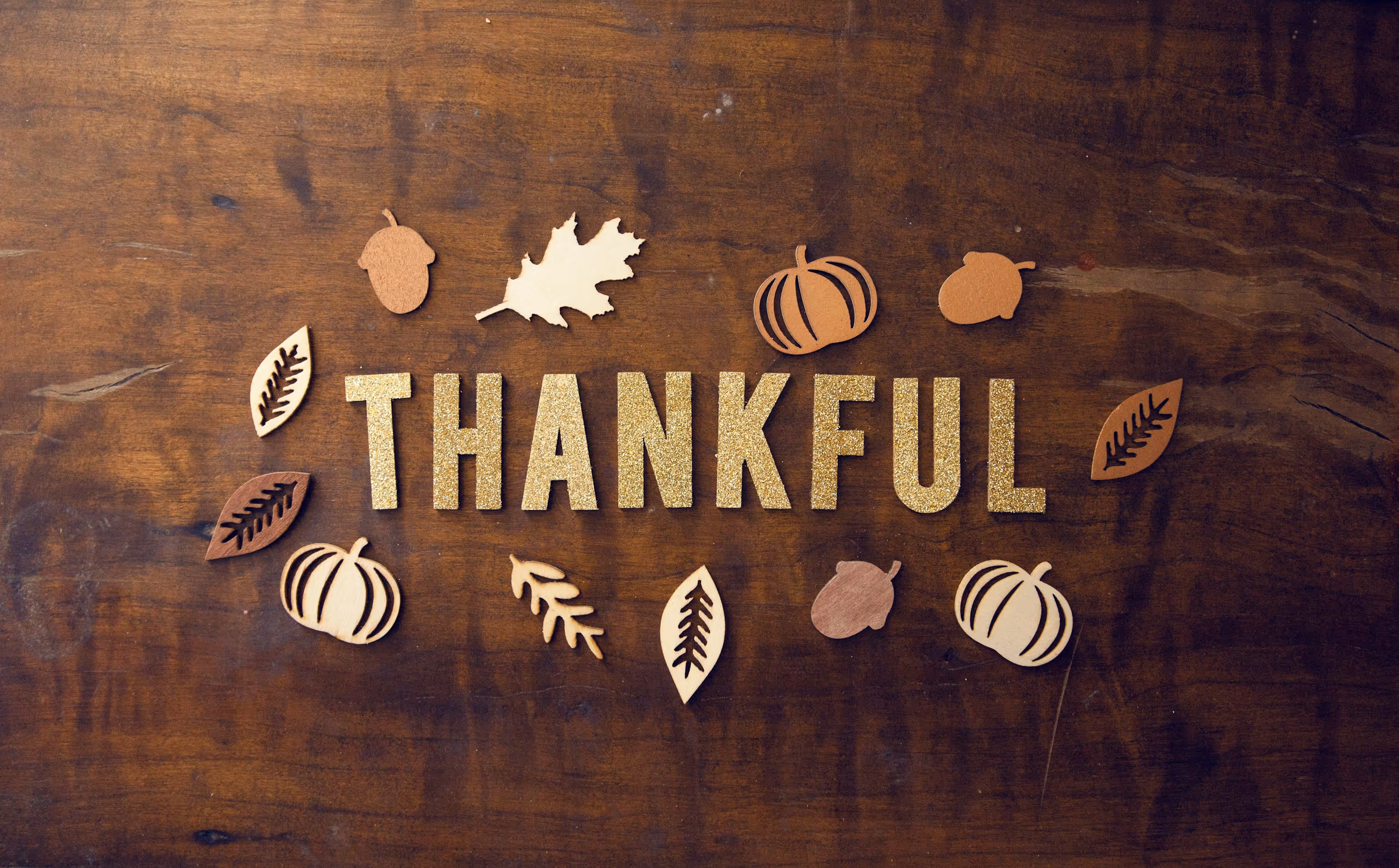 Thankful spelled out on a table surrounded by acorns, leaves, and pumpkins.